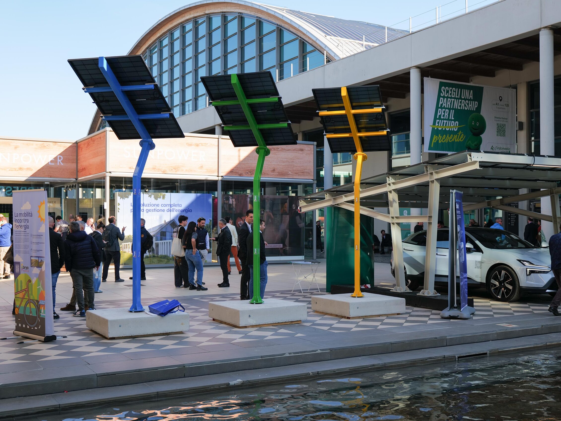 Inner courtyard of the expo centre with exposed colored solar panels and a car parked under a canopy with solar panels