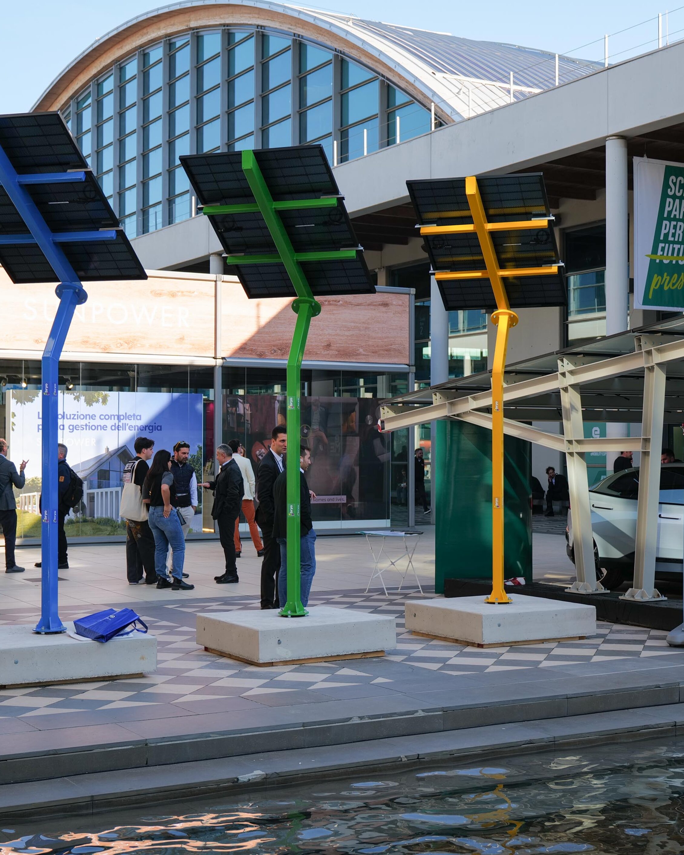 Inner courtyard of the expo centre with exposed colored solar panels and a car parked under a canopy with solar panels