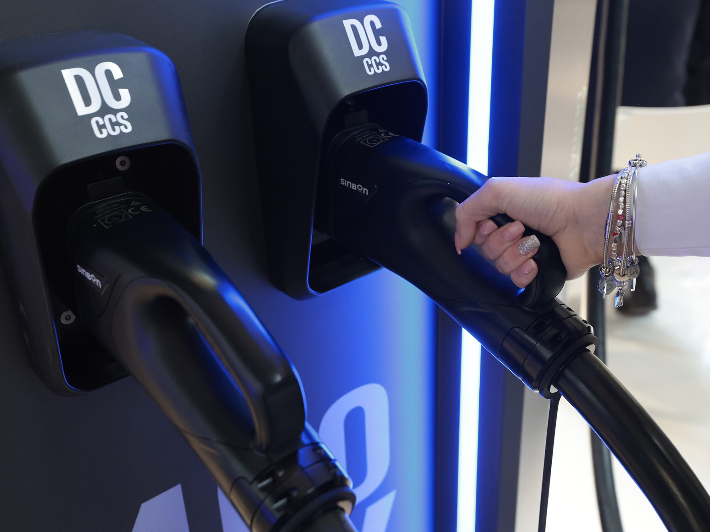 a hand grabbing a DC CCS fast charging connector for electric vehicles, installed on a display charging station inside the expo centre.