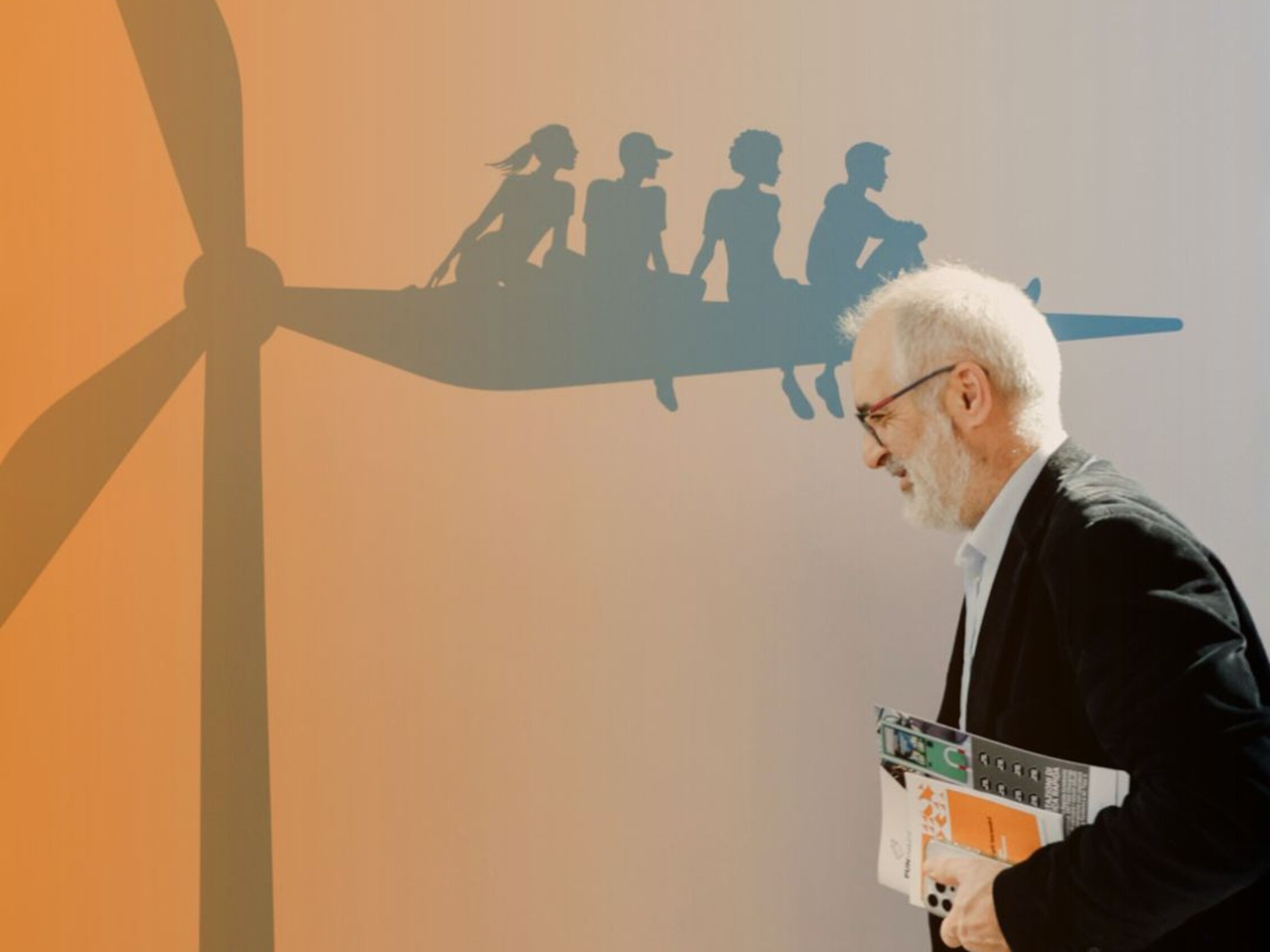A man walks past a wall illustration showing stylized people sitting on top of a wind turbine, with the text 'We circulate more and more clean energy'