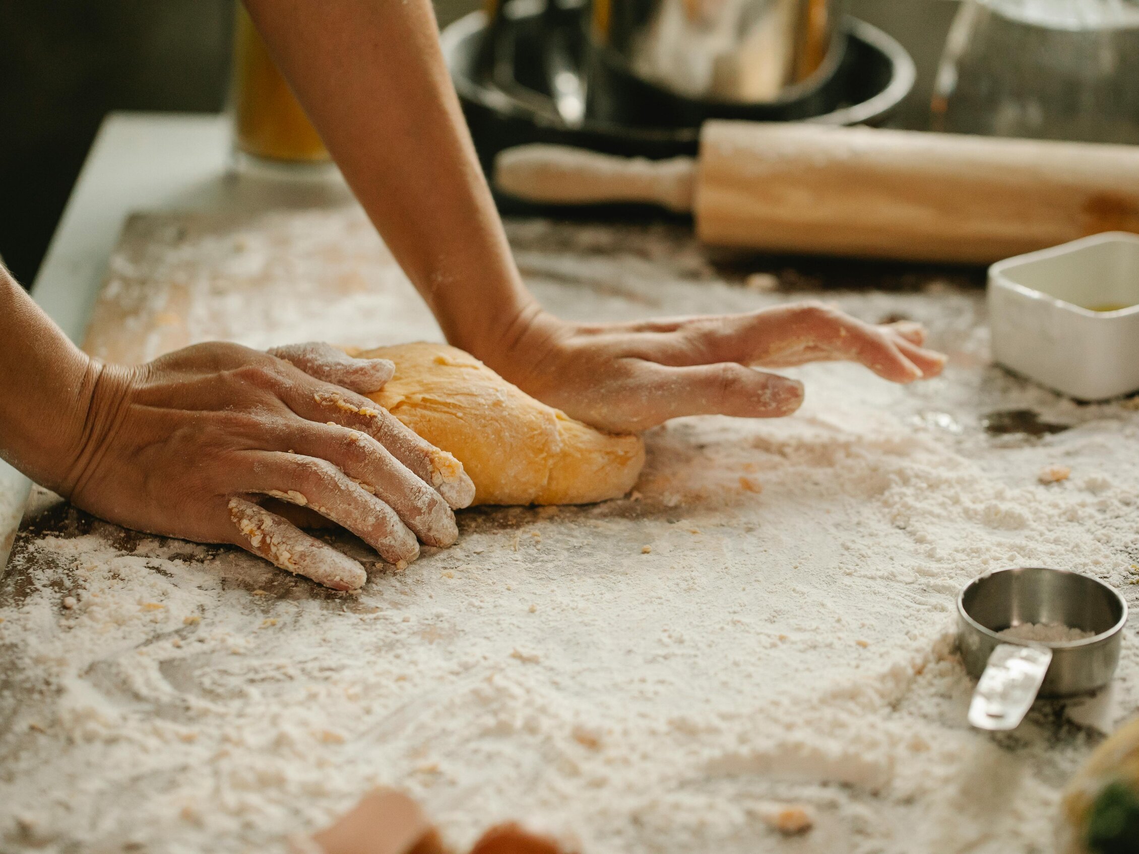  floured hands working a dough on a kitchen counter