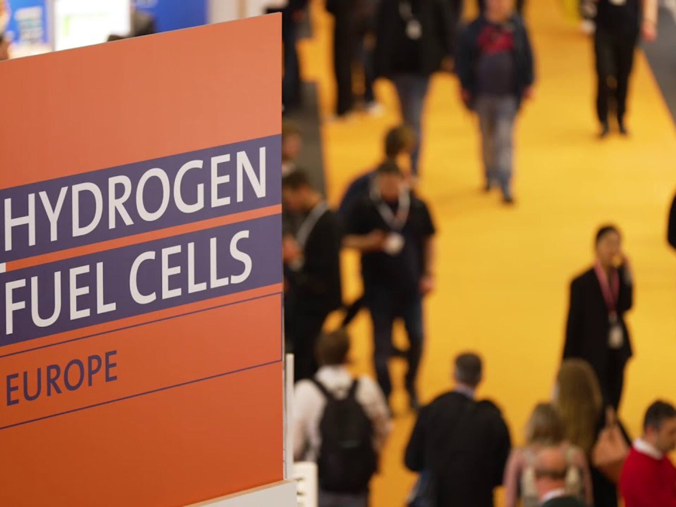 Sign with the words 'Hydrogen Fuel Cells Europe' inside the expo centre, with people walking in the background