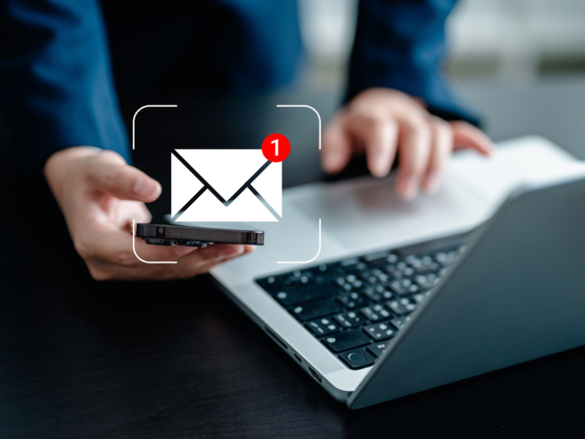 an email notification icon overlaying a man using both a smartphone and a laptop